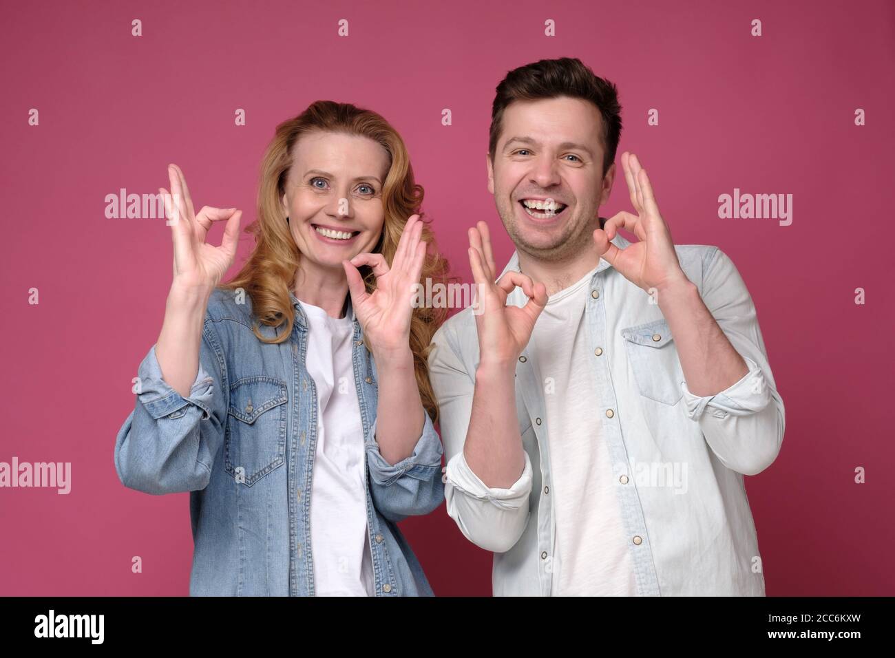 Uomo e donna sorridenti dal bell'aspetto che mostrano il segno OK con due mani. Foto Stock