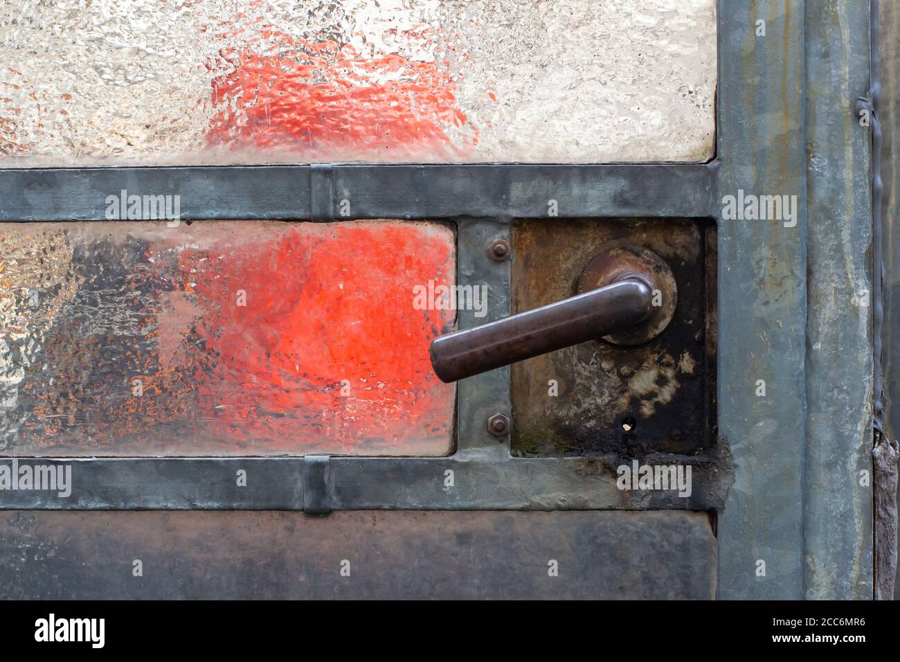Primo piano di una vecchia maniglia della porta arrugginita su un porta di vetro in una serra abbandonata Foto Stock