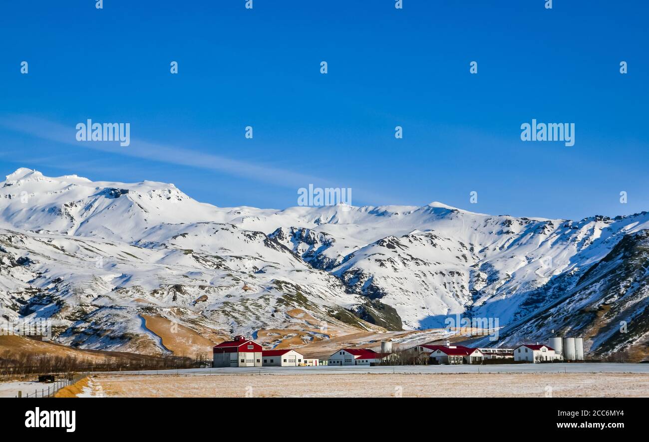 Thorvaldseyri fattoria edifici sotto il ghiacciaio Eyjafjallajökull in inverno, con cielo blu e sole, Islanda Foto Stock