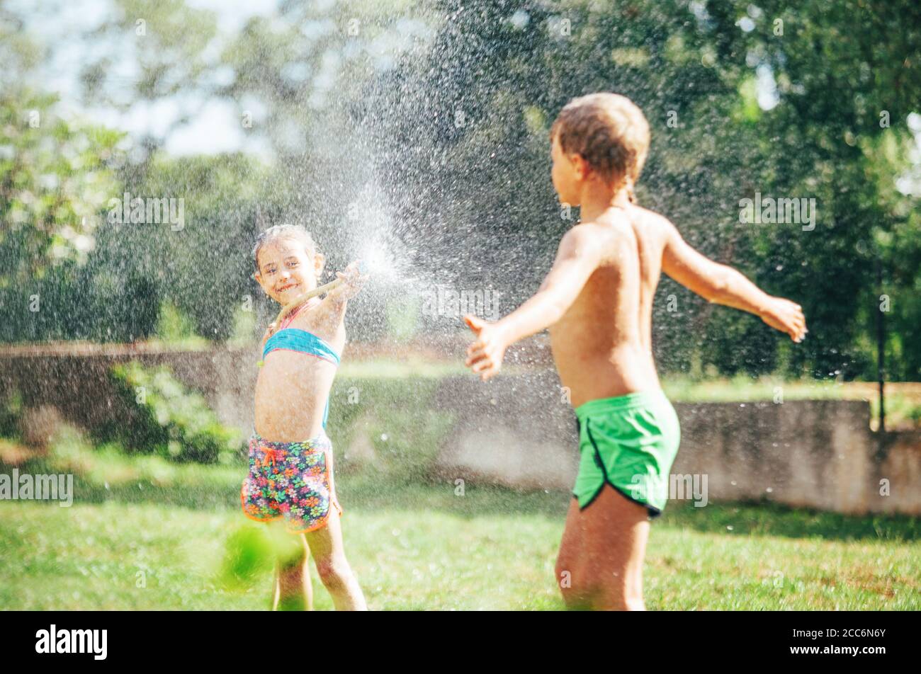 Fratello e sorella giocano insieme, rinfrescando con l'acqua spruzzata dalla casa del giardino Foto Stock