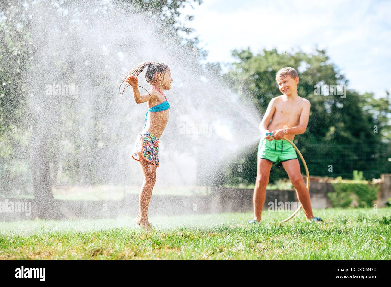 Fratello e sorella giocano insieme con il tubo di irrigazione in giardino Foto Stock
