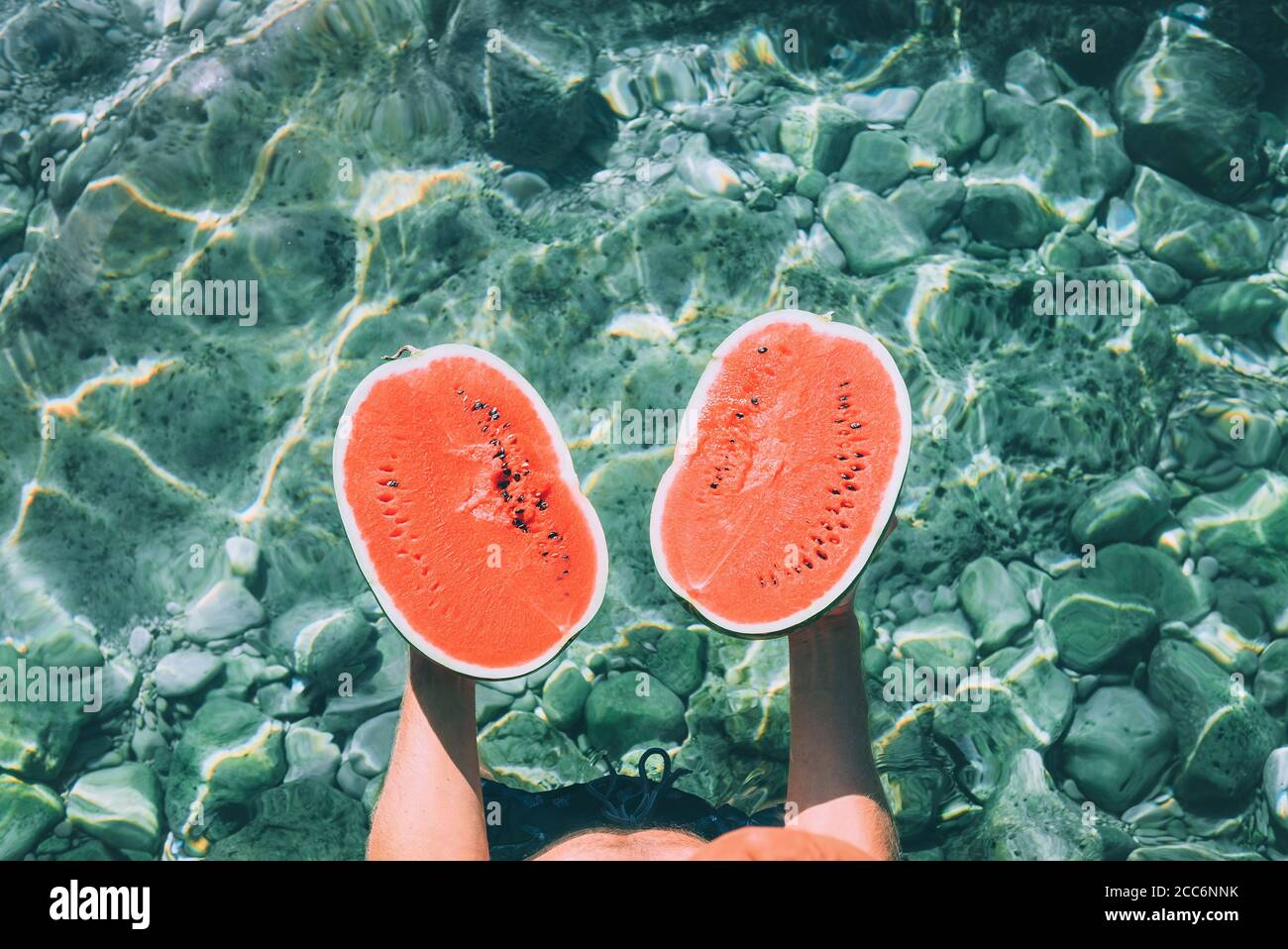 L'uomo tiene in mano due half di melone e si alza in piedi acqua di mare cristallina Foto Stock
