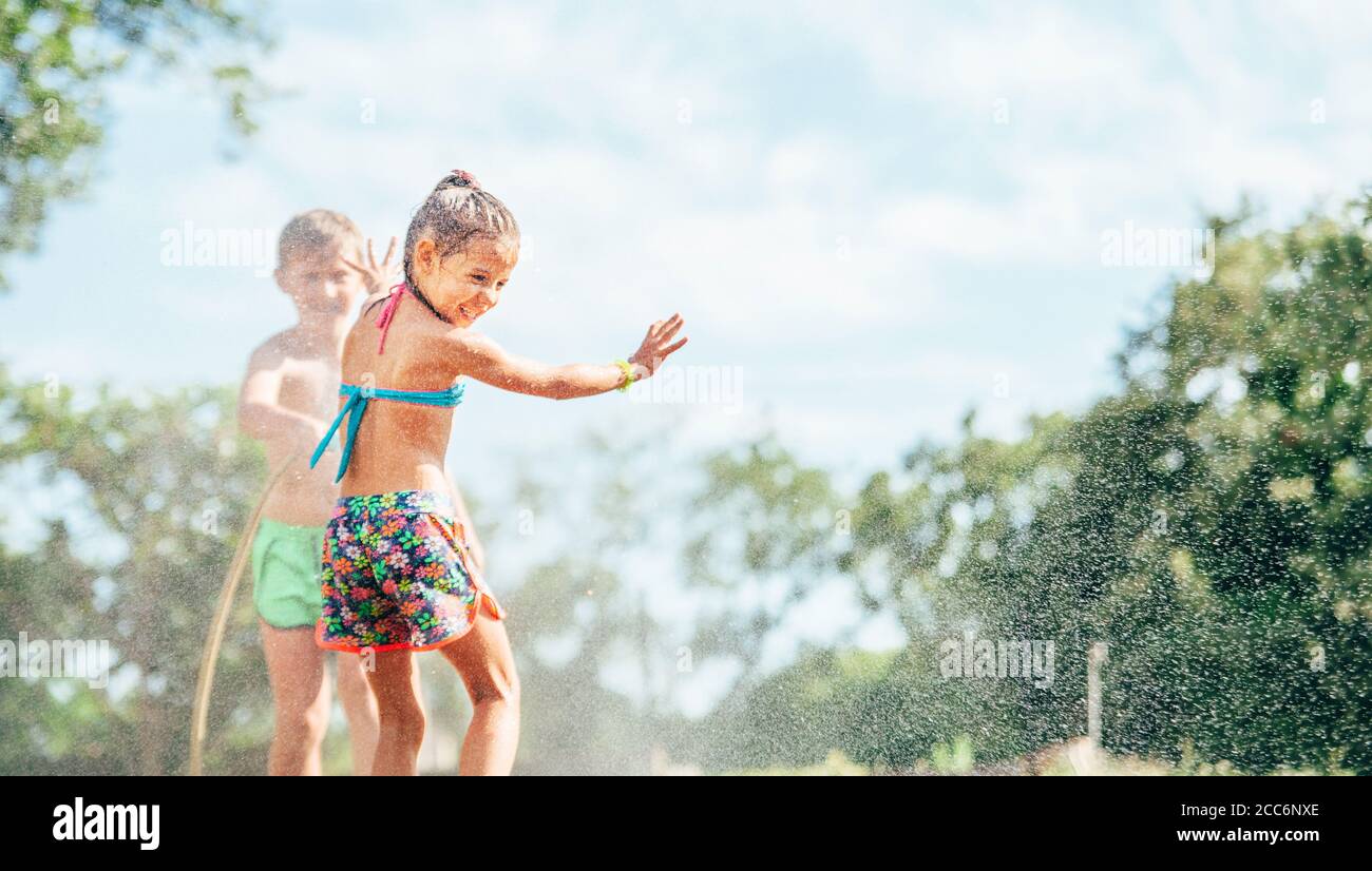 Due bambini giocano con acqua spruzzata nel giardino estivo Foto Stock