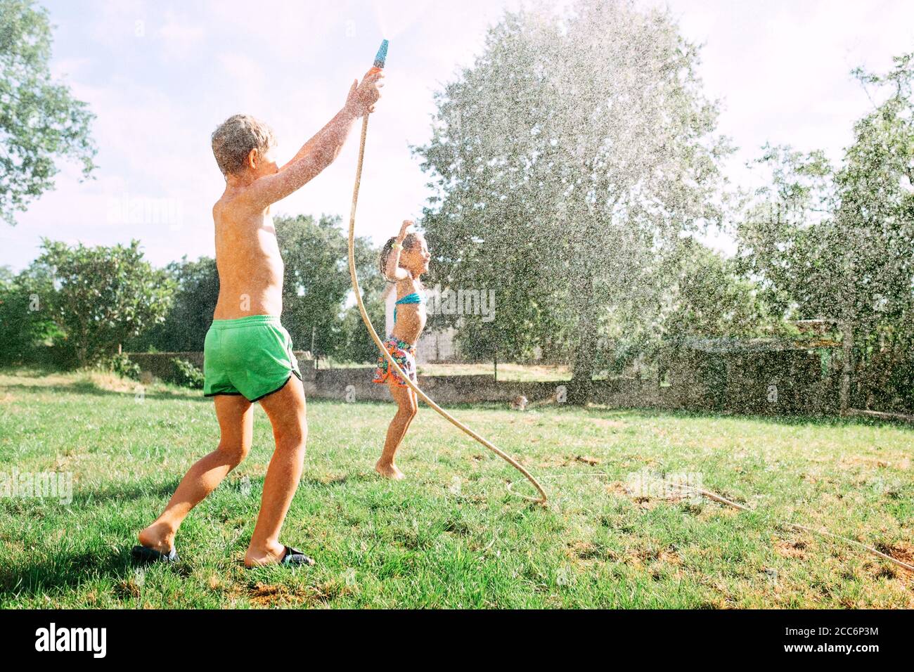 Due bambini giocano insieme in giardino, caldo giorno d'estate, fanno un raim da giardino annaffiatura tubo Foto Stock