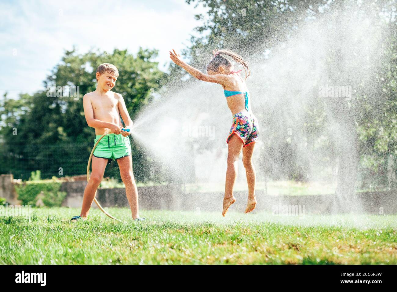 Due bambini giocano in giardino, si riversa l'un l'altro dal tubo, fa una pioggia Foto Stock
