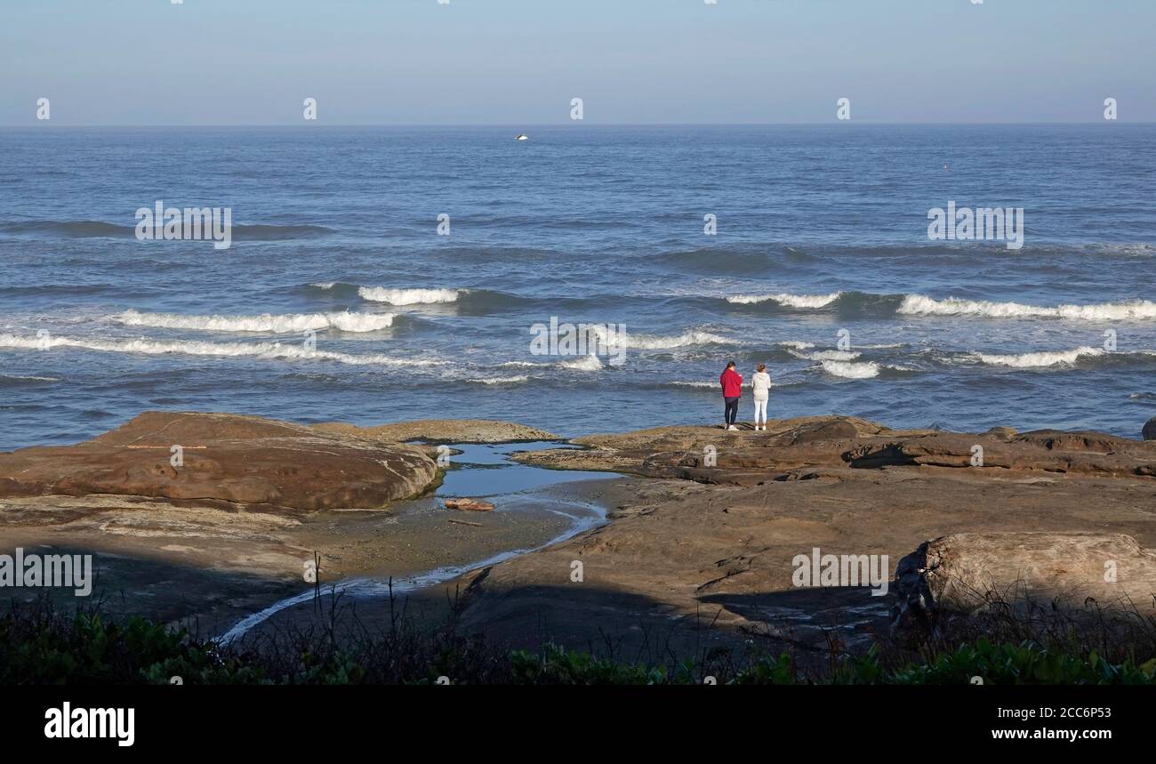 Due donne si trovano su una vista rocciosa sopra l'Oceano Pacifico su un sentiero oceanico nella piccola città di Yachats, Oregon. Foto Stock