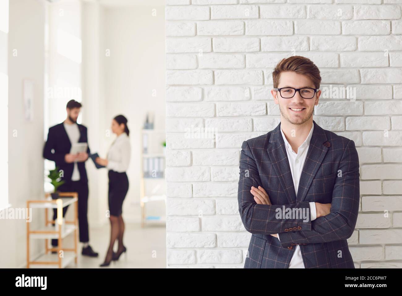 Sorridente uomo d'affari positivo in abbigliamento casual in piedi in un ufficio bianco su un muro bianco. Foto Stock