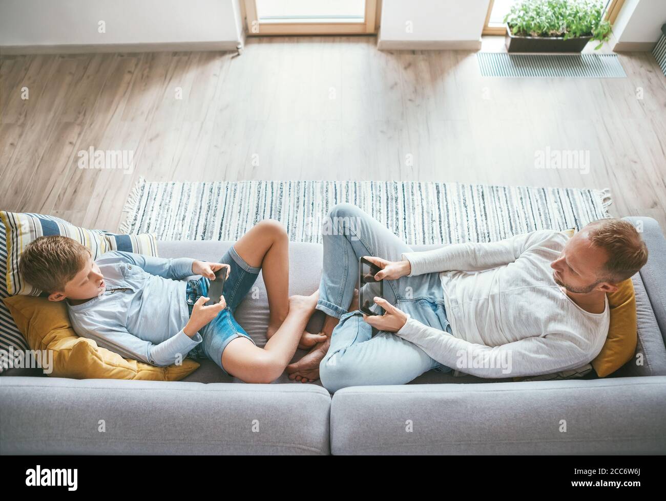 Padre e figlio Losted in dispositivi elettronici. Giocano con tablet e gamepad seduti in salotto Foto Stock