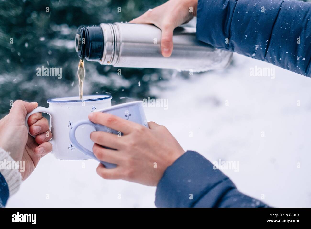 Mani con tazze di tè e thermos in fiasca innevata immagine ravvicinata della foresta invernale Foto Stock