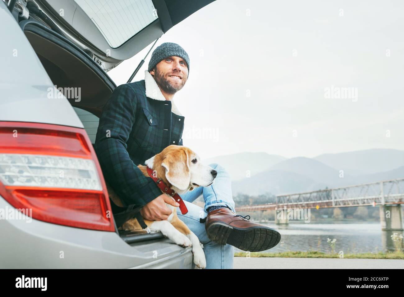 Uomo con cane beagle seduto insieme nel bagagliaio dell'auto. Nel tardo autunno viaggia con il concetto di animali domestici. Foto Stock