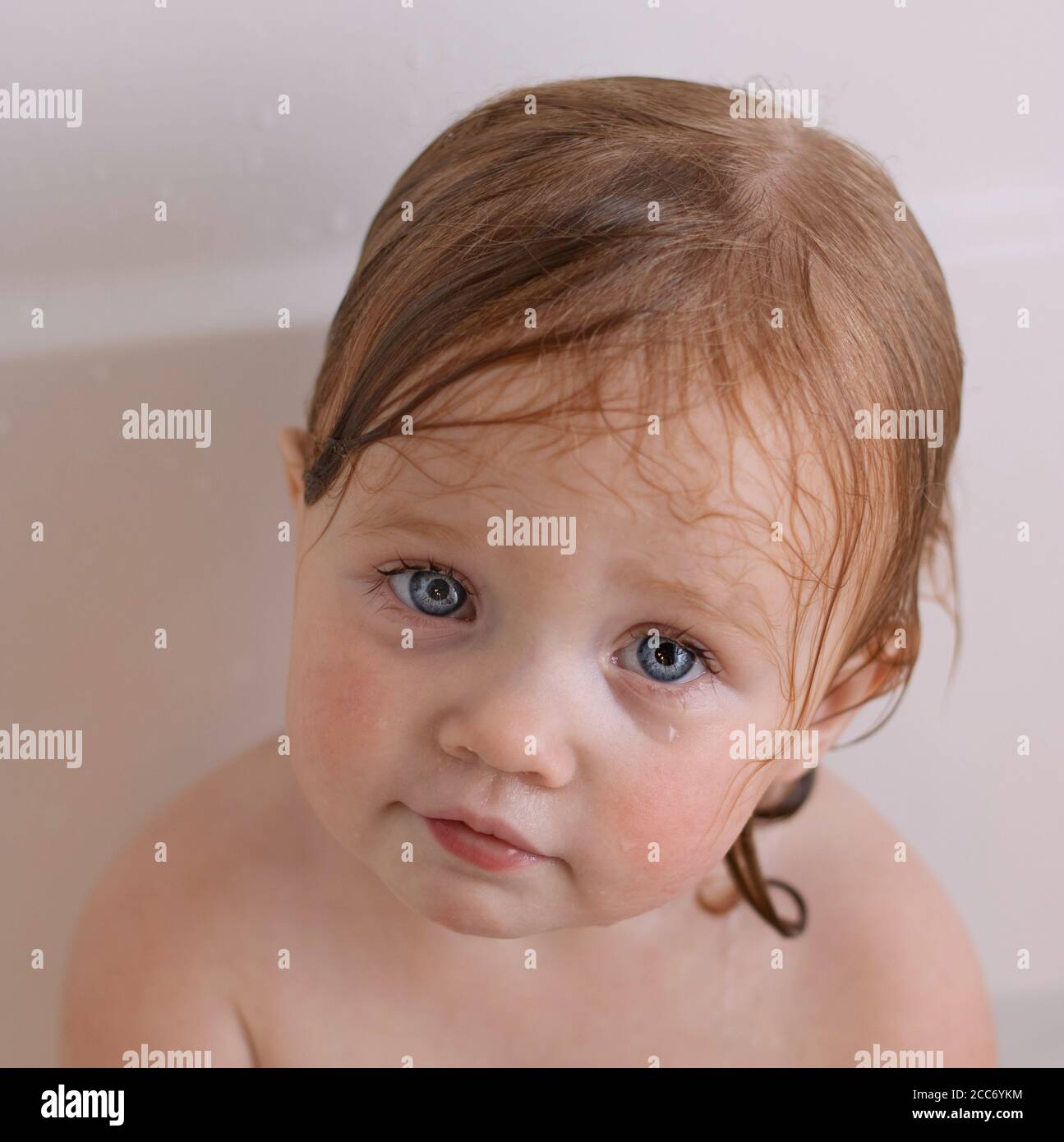 Bambina con grandi occhi blu nella vasca da bagno con capelli bagnati Foto Stock