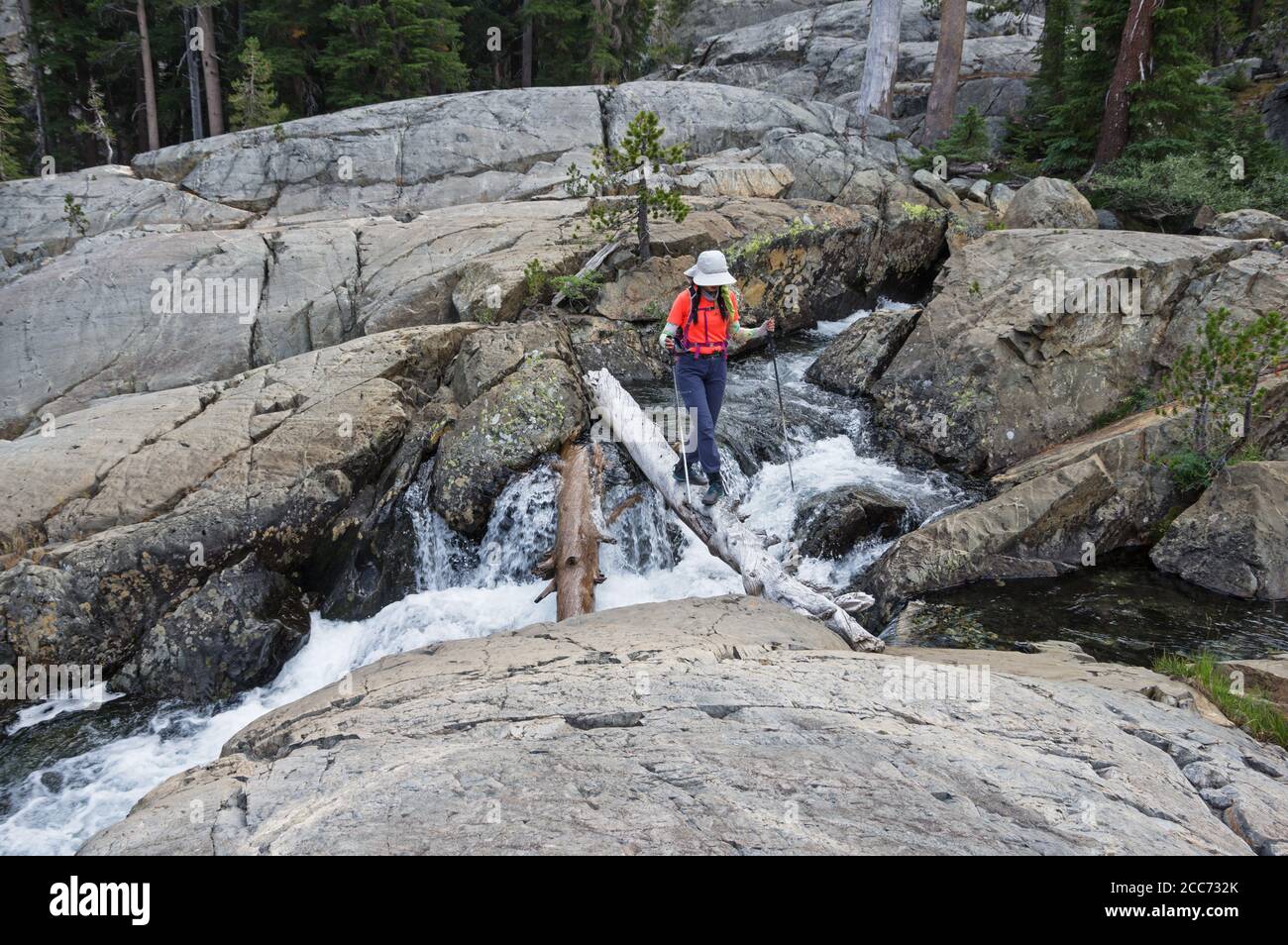 donna escursionista che attraversa un ruscello attraverso rocce glaciali lucidate su un registro Foto Stock