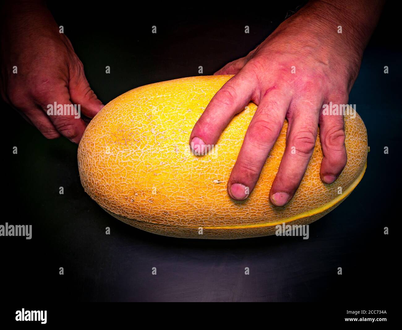 Un melone giallo tagliato con un coltello nelle mani di un uomo. Foto Stock