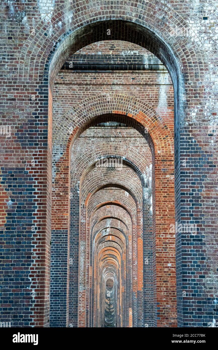 Vista attraverso gli archi del Viadotto della Valle di Ouse (Viadotto Balcombe) che porta la linea ferroviaria di Londra a Brighton sul fiume Ouse a Sussex, Regno Unito Foto Stock
