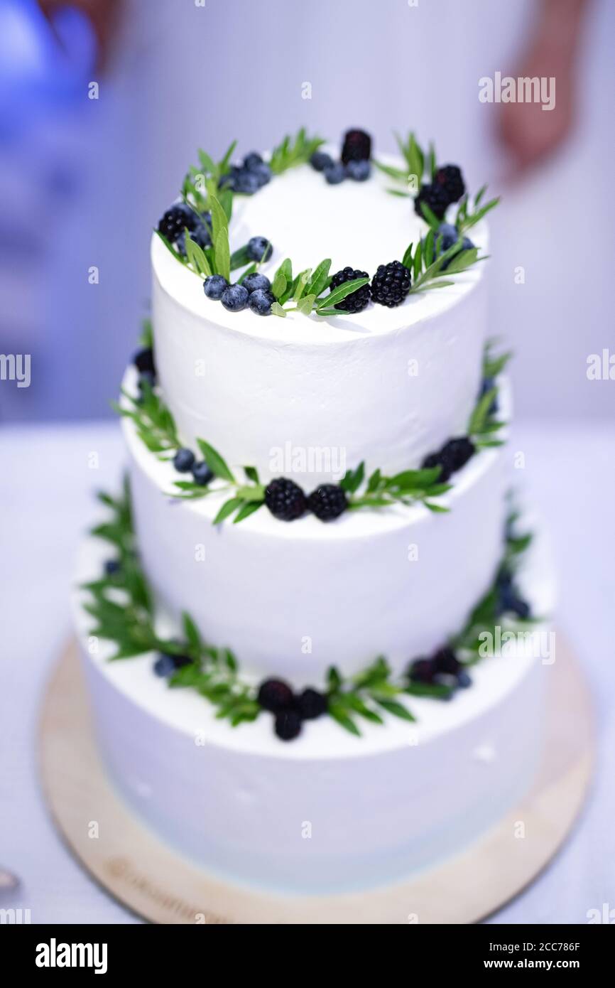 torta bianca a tre livelli decorata con more e foglie , fuoco selettivo, torta nuziale Foto Stock