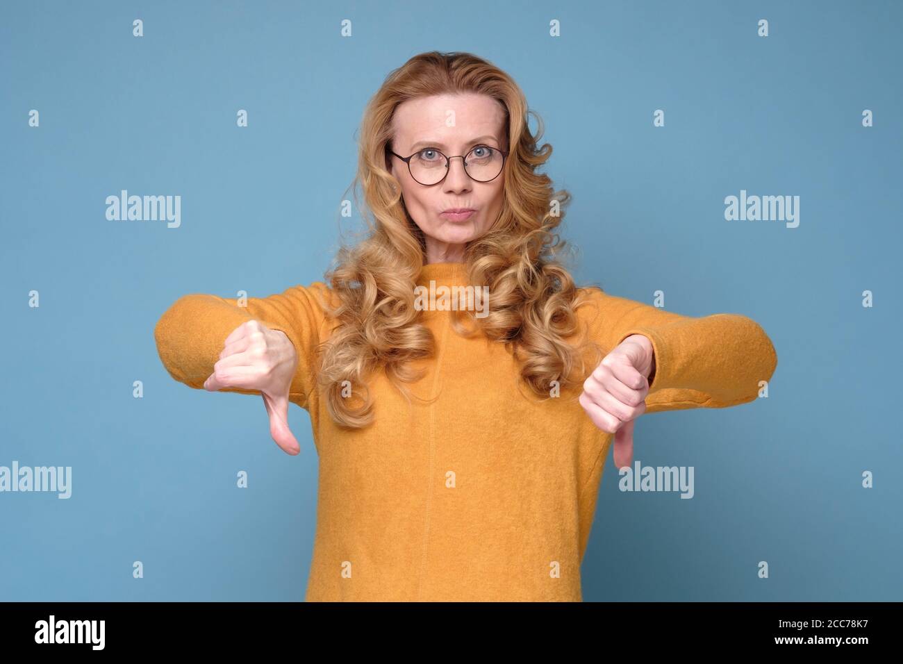 La donna matura, cupa e insoddisfatta, guarda i pollici della fotocamera verso il basso. Foto Stock