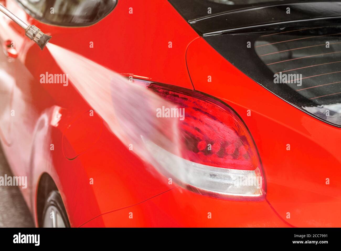Luce posteriore della vettura rossa lavata in autolavaggio, spruzzatura d'acqua sulla superficie Foto Stock