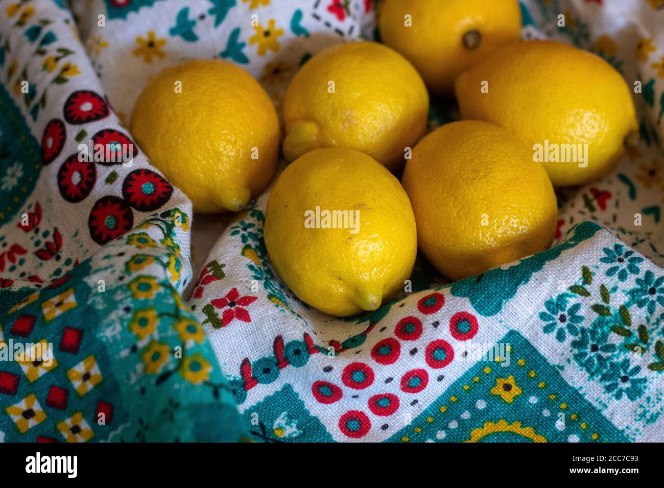 Mazzo di limoni su tovaglia colorata seduta sul tavolo con sfondo marrone sfocato Foto Stock