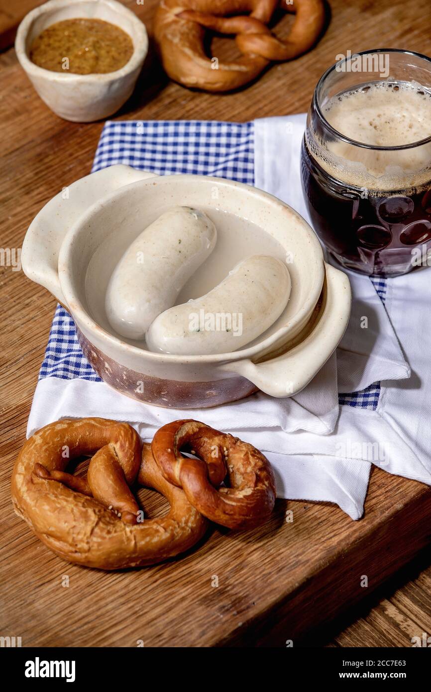 A Monaco le tradizionali salsicce bianche bavaresi in padella di ceramica vengono servite con senape dolce tedesca, tazza di birra scura e pane pretzel su napk bianco e blu Foto Stock