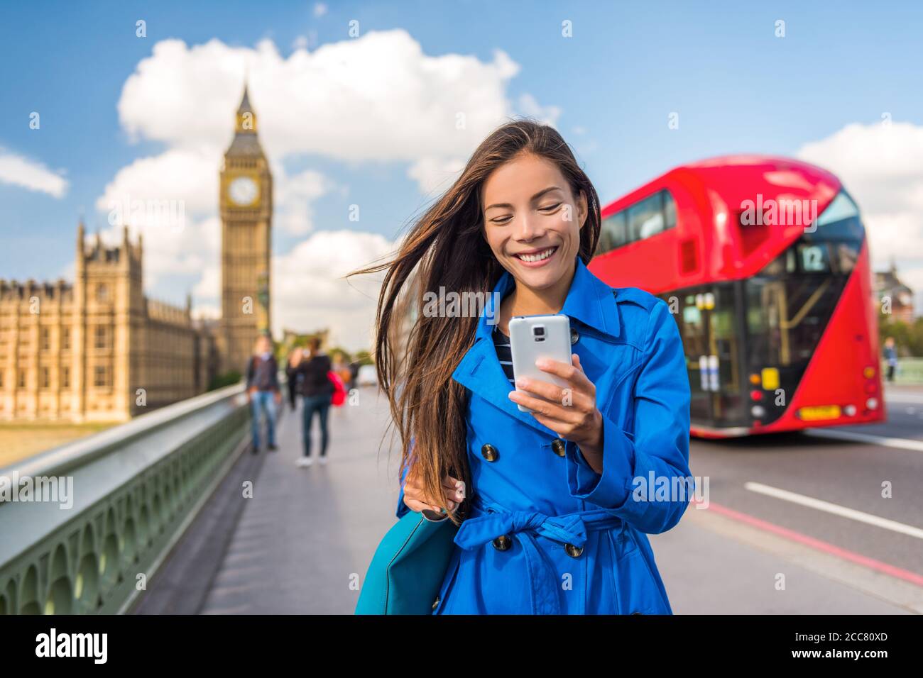 Telefono di Londra donna di affari SMS su smartphone app mobile per il pagamento o lo shopping online. Città urbana stile di vita asiatica ragazza felice camminare sul Big ben Foto Stock