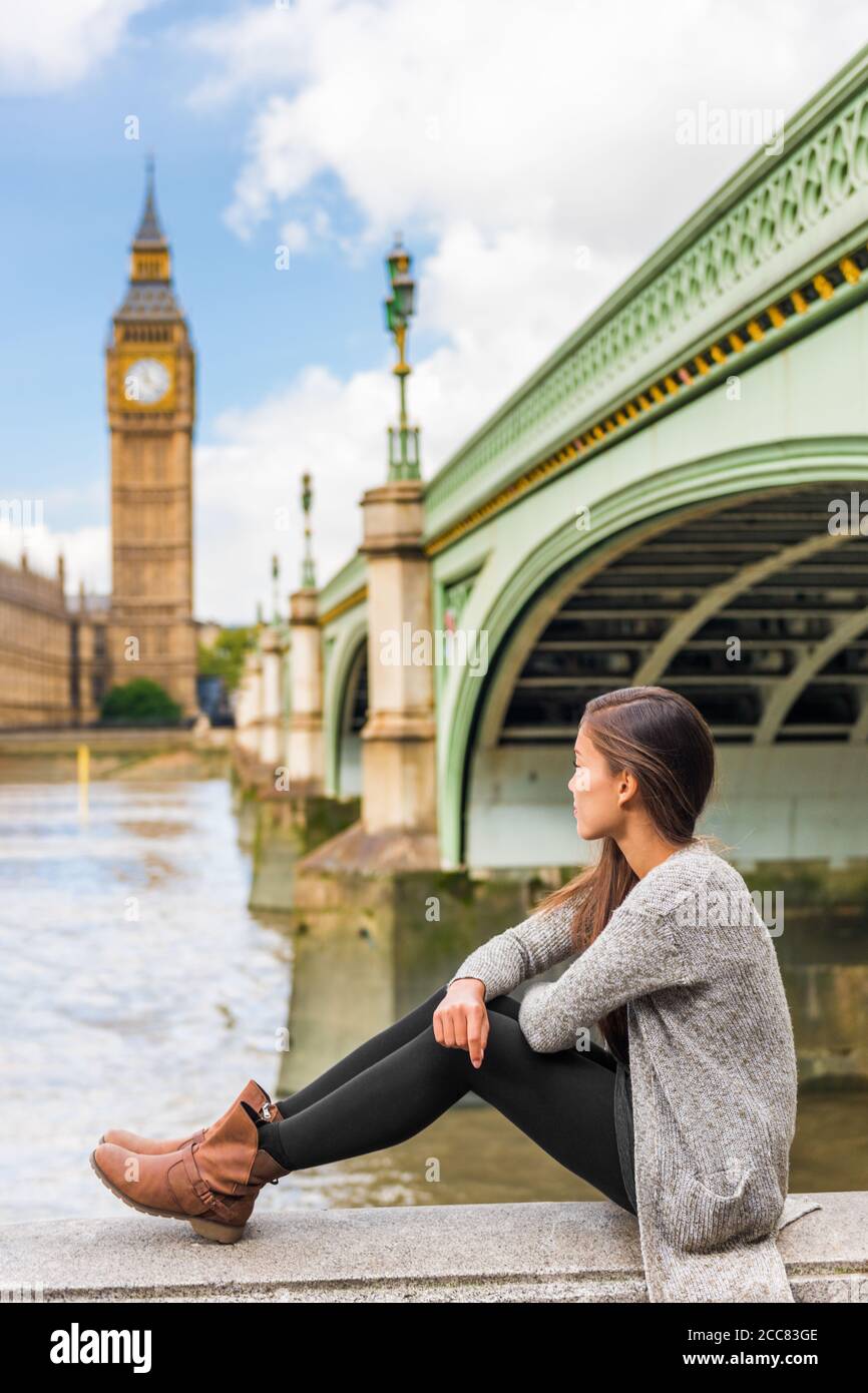 Londra città Europa viaggio destinazione giovane donna rilassante pensiva guardando Big ben torre orologio. Ragazza britannica asiatica seduta in autunno all'aperto Foto Stock