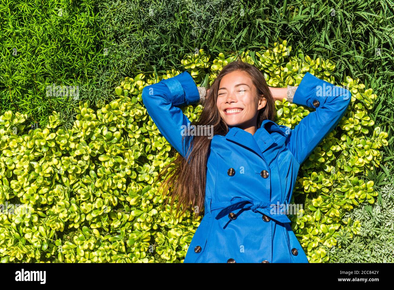 Natura relax Felice primavera camice donna sdraiato su fondo verde erba texture. Asian sorridente ragazza in stile giacca moda Foto Stock