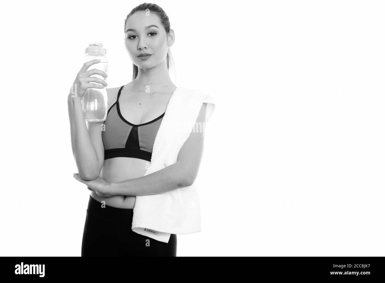 Studio shot del giovane bella donna asiatica tenendo la bottiglia di acqua con un asciugamano sopra la spalla pronto per la palestra Foto Stock