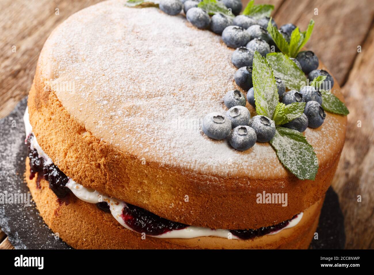La ricetta della torta di Spagna Victoria combina la marmellata di mirtilli e la crema di chiocciole sulla tavola di ardesia sul tavolo. Orizzontale Foto Stock