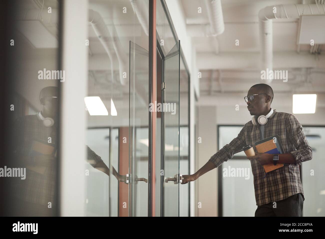 Giovane africano in abbigliamento casual che apre la porta di sala del consiglio che viene alla riunione Foto Stock
