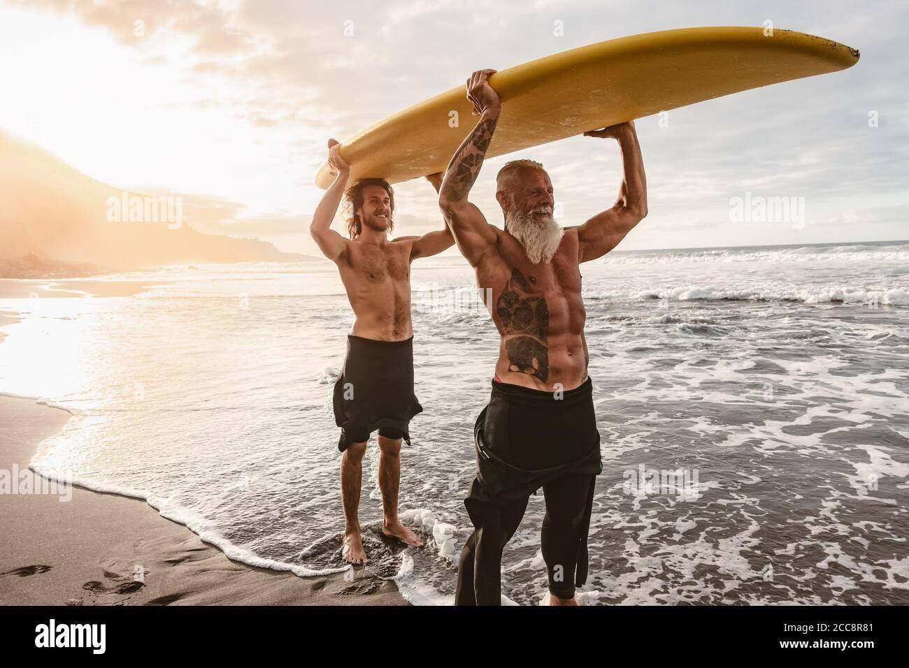 Amici felici con diverse età surf insieme sull'oceano tropicale - persone sportive che si divertono durante la giornata di surf vacanze Foto Stock