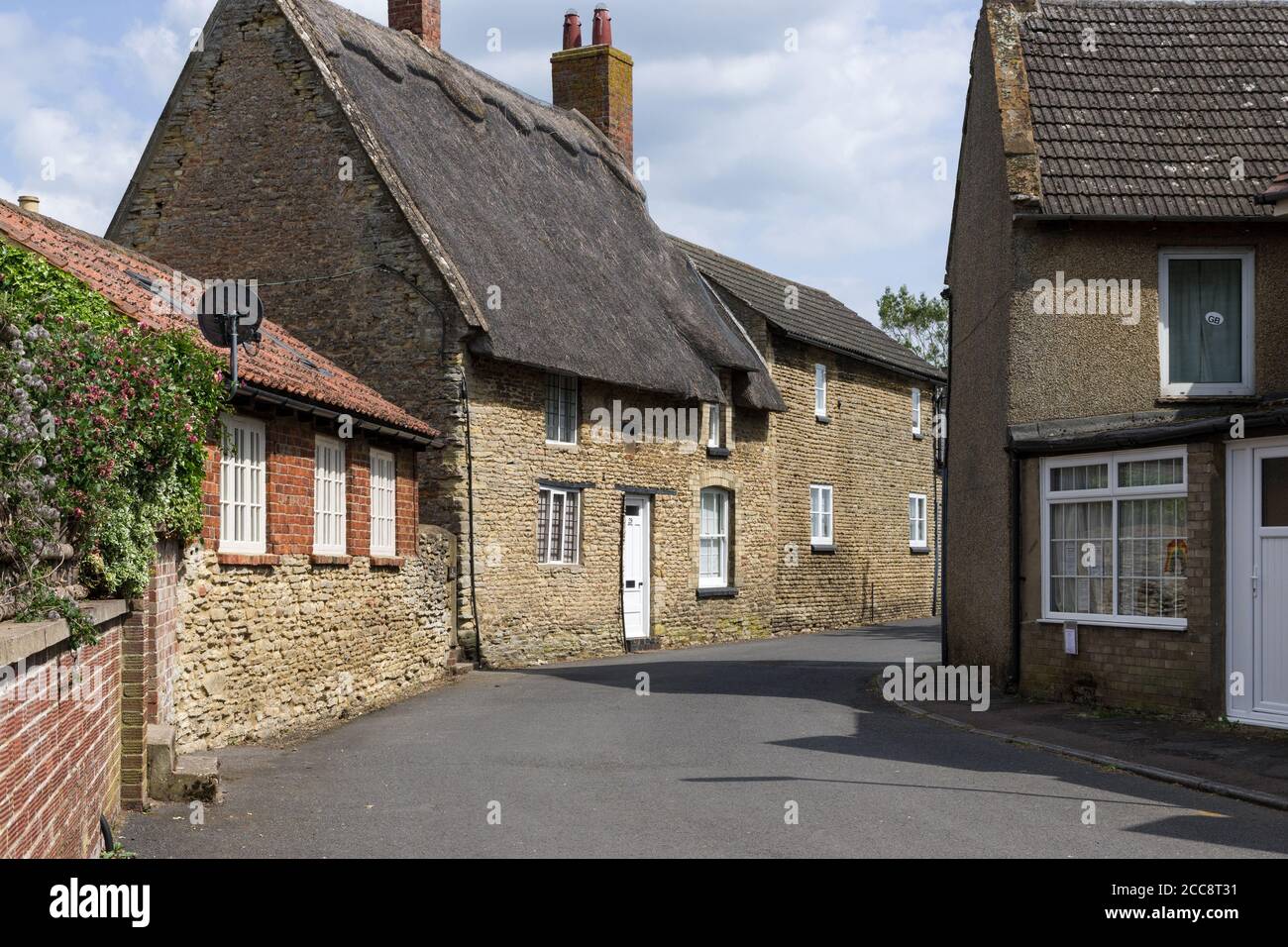 Vista sulla strada in estate nel villaggio di Bozeat, Northamptonshire, Regno Unito; con case in pietra, con tetto di paglia. Foto Stock