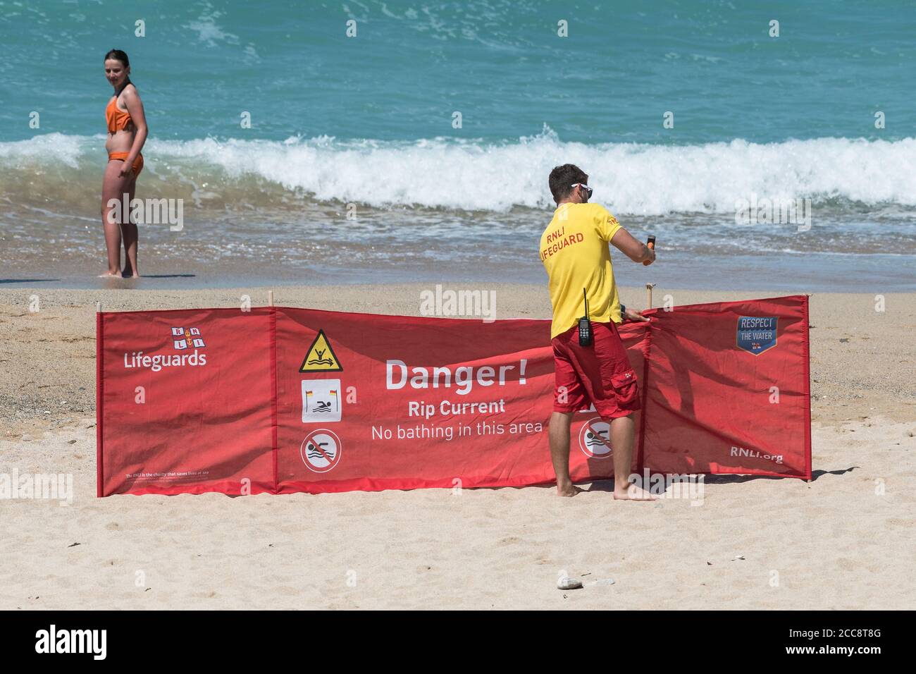 Un Lifeguard RNLI che ha messo un cartello di avvertimento su Fistral Beach a Newquay in Cornovaglia. Foto Stock