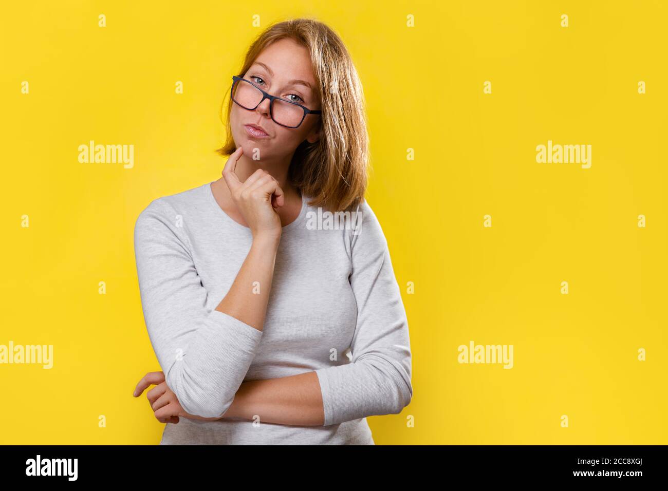 Ritratto di una bella bionda con occhiali, che guarda pensieroso. Sfondo giallo. Foto Stock