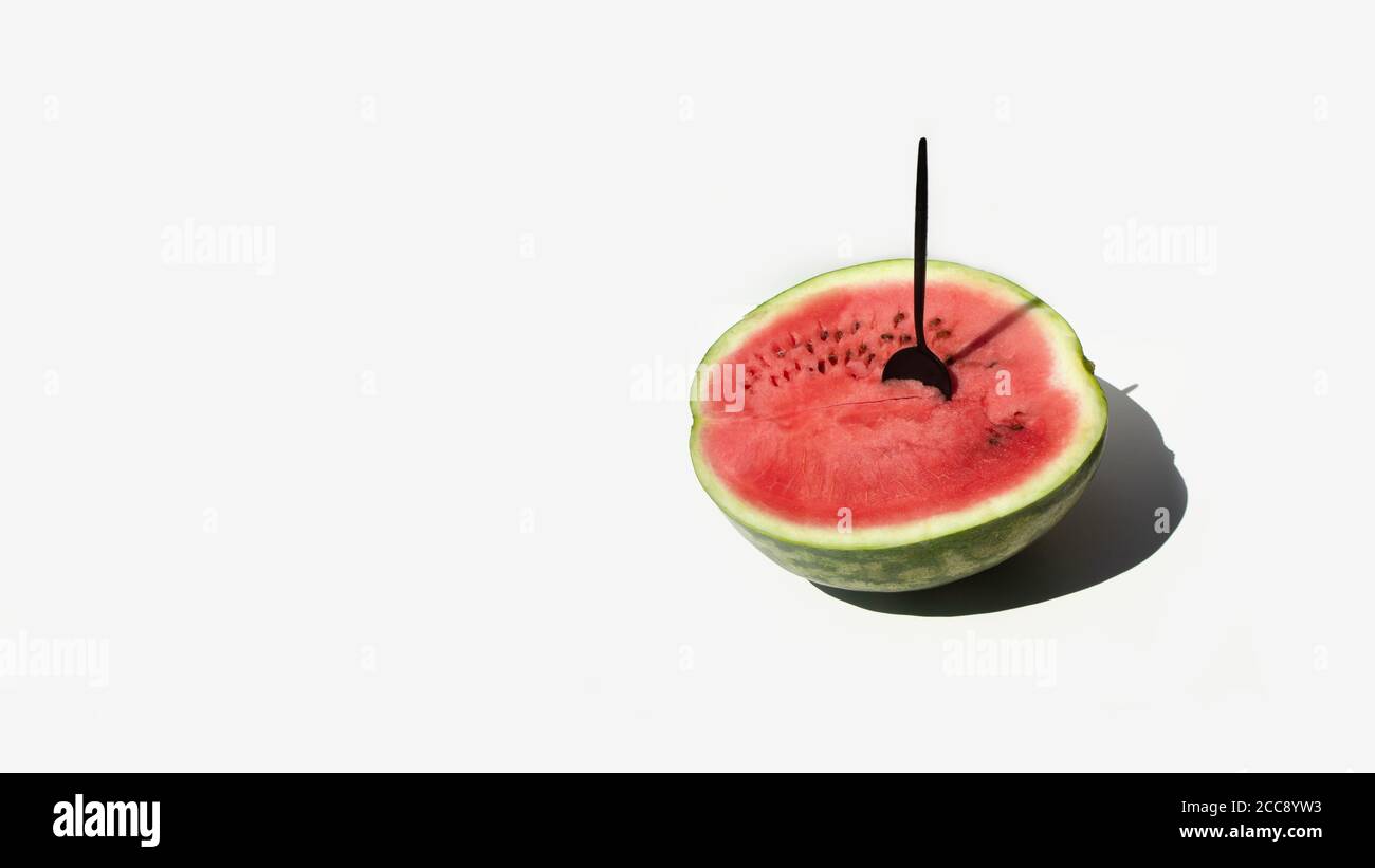 Un cucchiaio da tavola inserito in un cocomero mezzo maturo su sfondo bianco. Concetto di frutta estiva minimo. Foto Stock