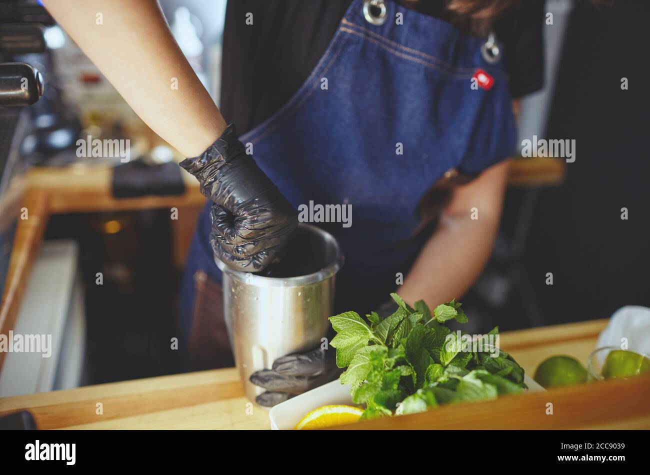 Barista che indossa guanti medici in lattice nero, rendendo mojito cocktail.Mint foglie, ingrediente per bevande al bar Foto Stock