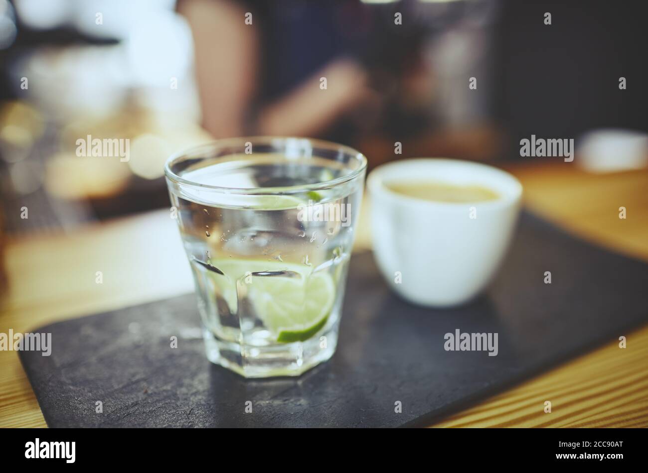 Immagine sfocata della piastra di pietra con una tazza di caffè e. Acqua in un bicchiere con calce al bar counter.Coffee break Foto Stock