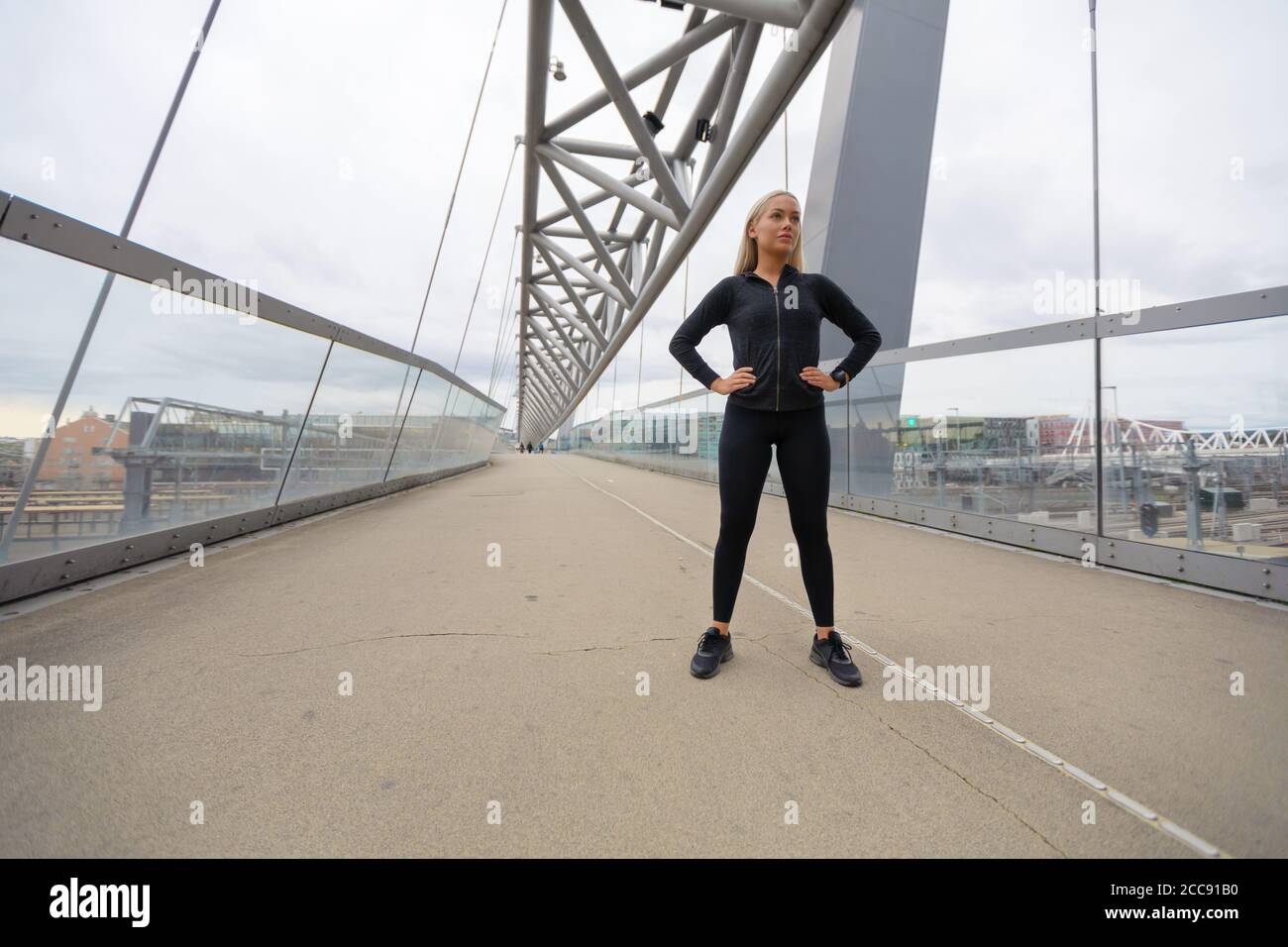 Fiducioso donna con le mani sui fianchi in abito di Allenamento in piedi sul ponte Foto Stock