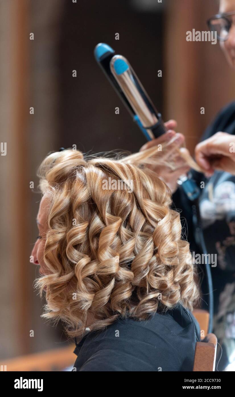Acconciatura. Piastra per capelli sui capelli biondi della sposa Foto Stock