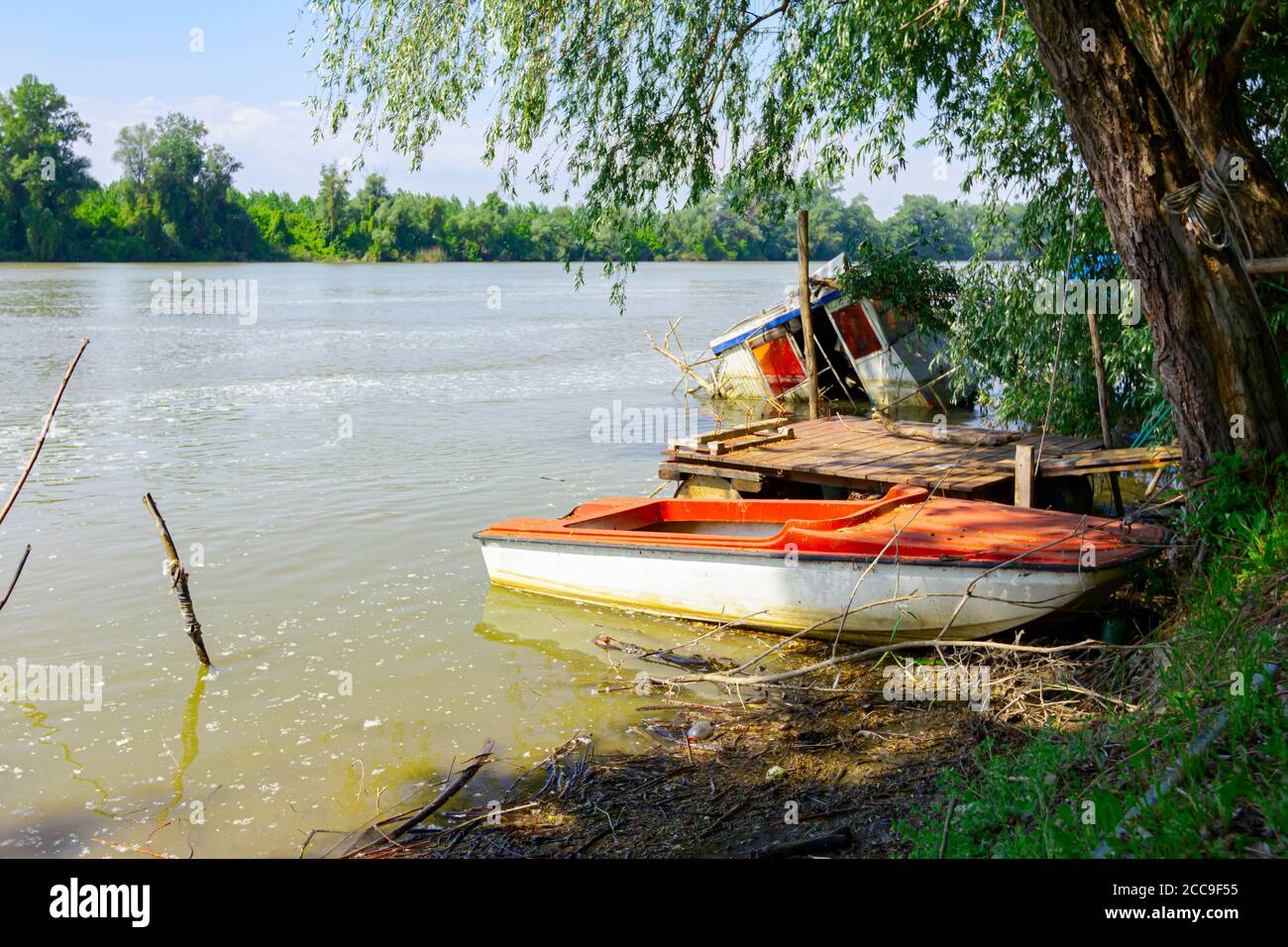 Una piccola barca da pesca distrutta è parzialmente allagata, che si trova sulla costa di un ampio fiume. Foto Stock