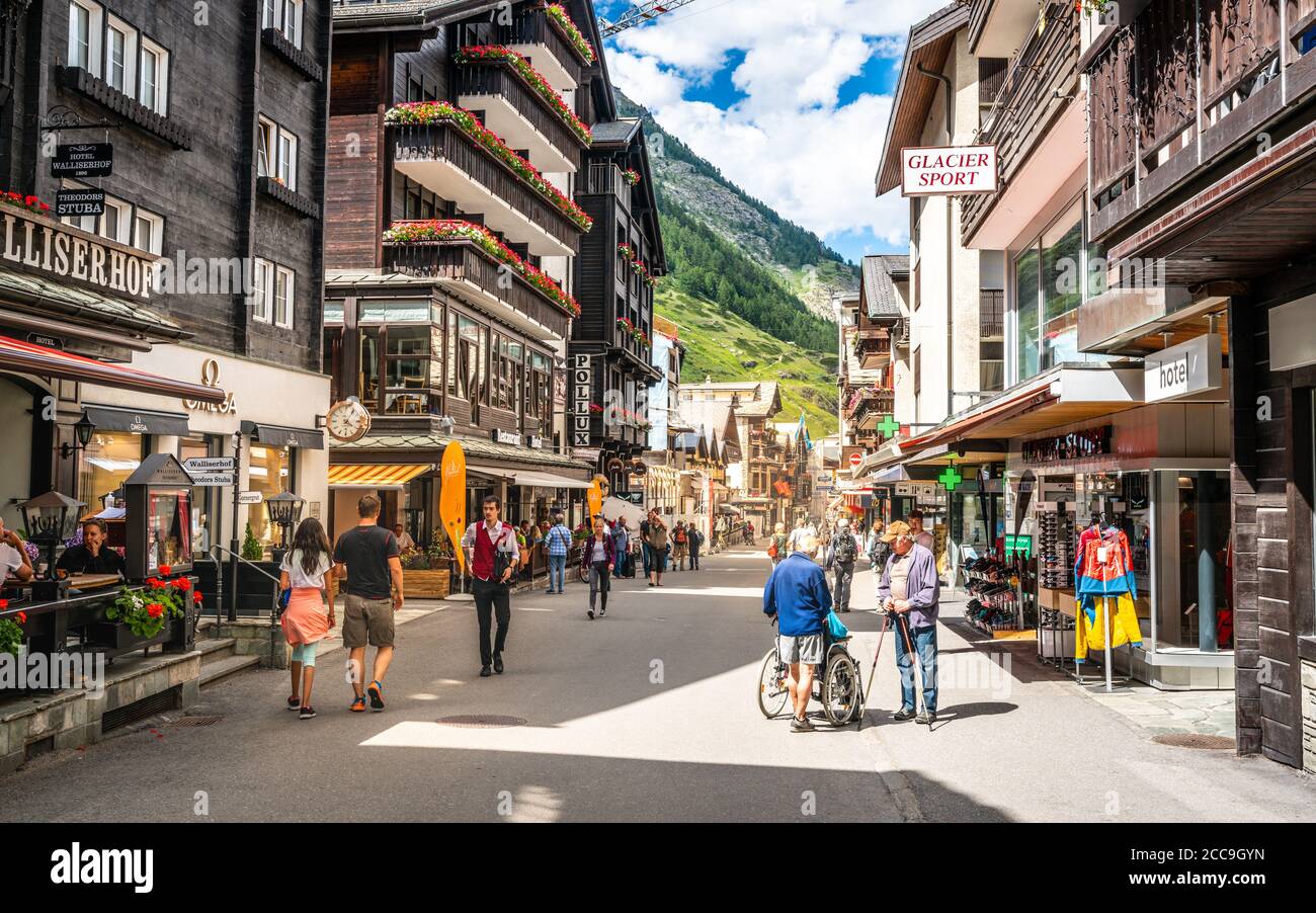 Zermatt Svizzera , 2 luglio 2020 : Zermatt Bahnhofstrasse strada principale dello shopping piena di persone con vecchie case svizzere in legno e drammatica luce durante Foto Stock