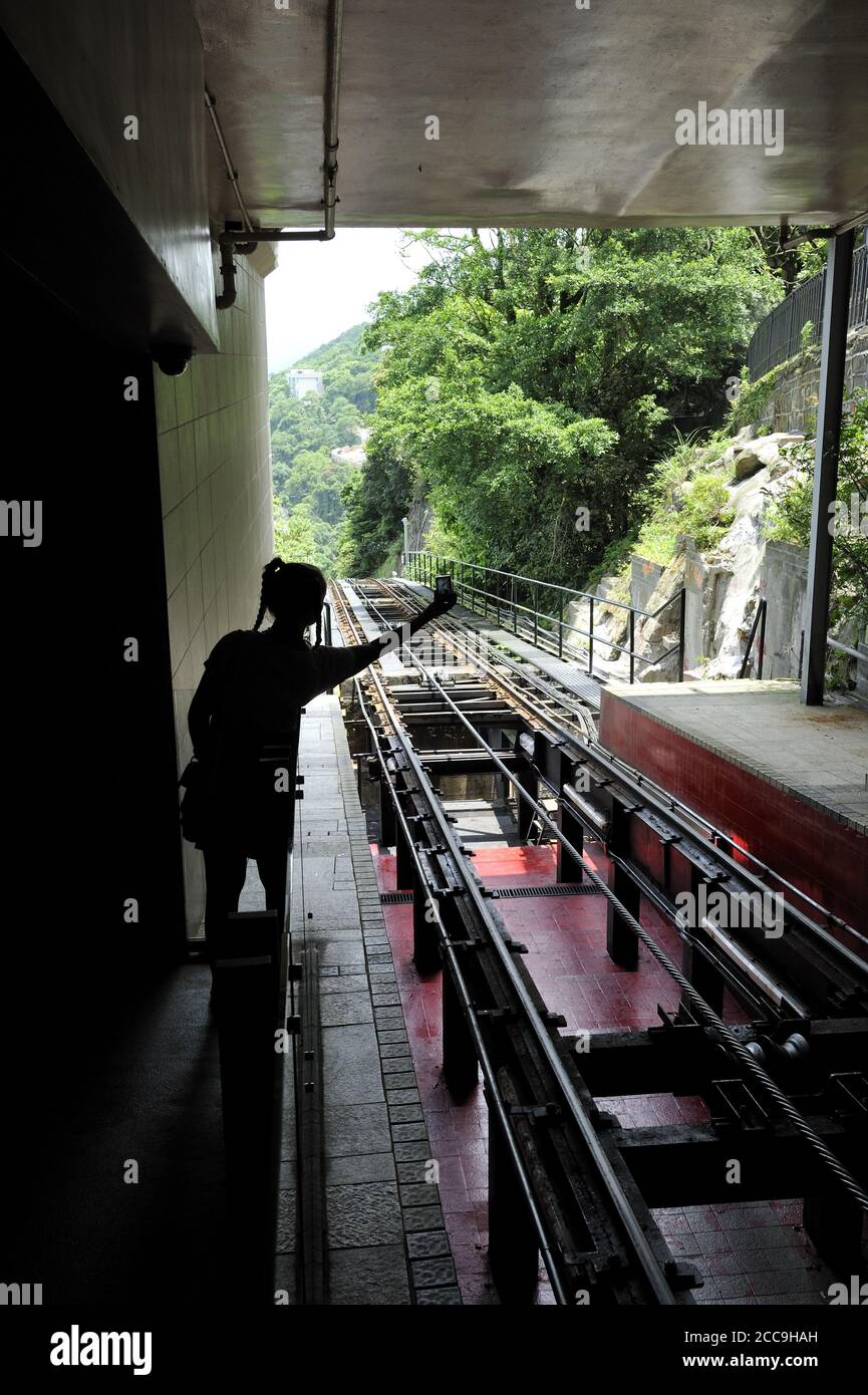 Silhouette di una ragazza adolescente che scatta una foto della pista della Peak Tramway di Hong Kong, una funicolare che trasporta le persone da e per il Peak. Foto Stock