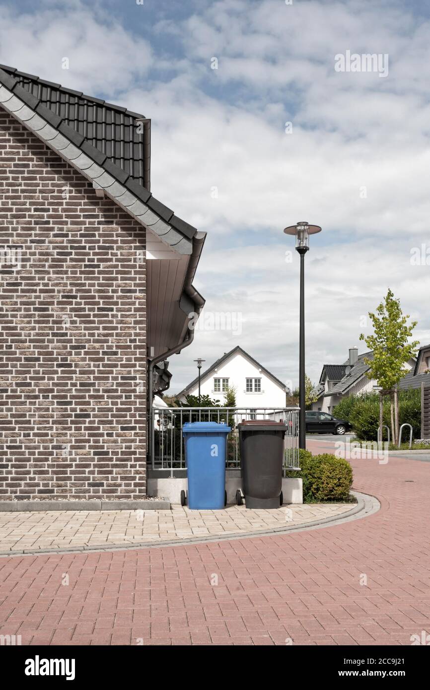 Vista ad angolo basso della strada suburbana, rifiuti e bidoni di riciclaggio di carta accanto alla casa con facciata in mattoni in primo piano Foto Stock