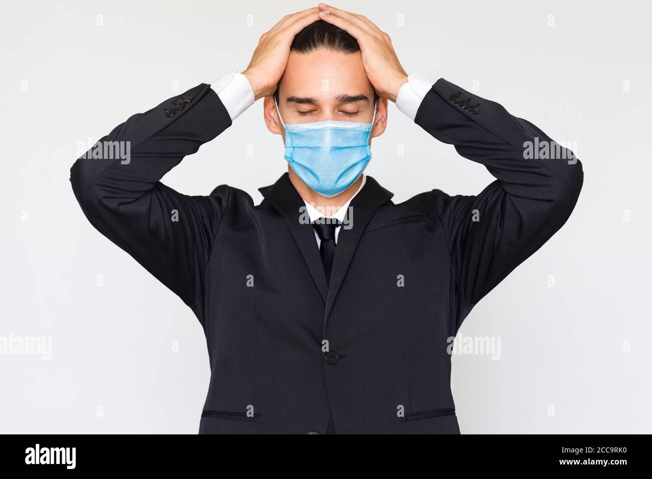 Pressione di lavoro e overworked - uomo d'affari stressato con le mani sulla testa che indossa una maschera medica del viso. Isolato su uno sfondo bianco. Foto Stock