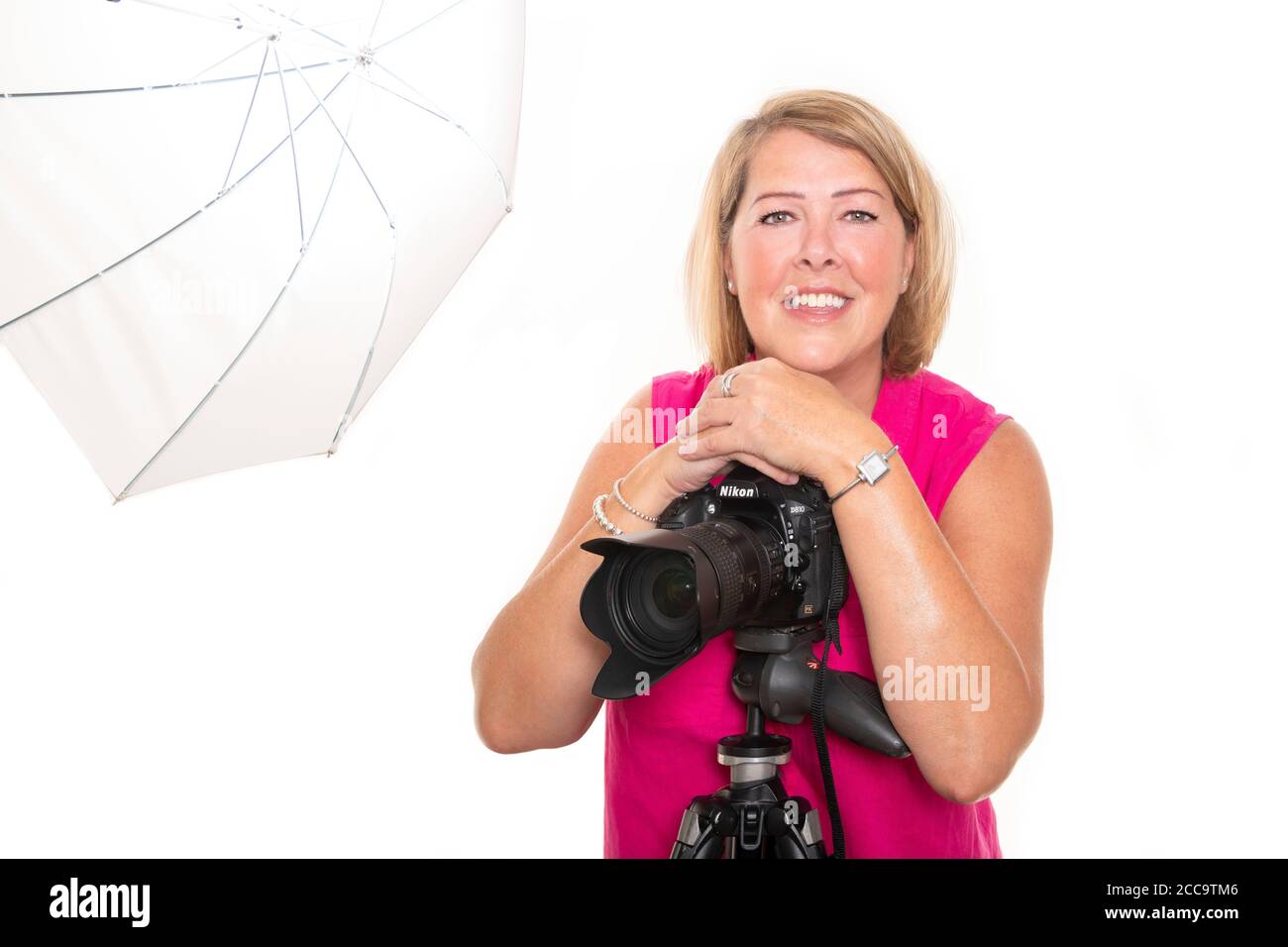 Ritratto orizzontale di un fotografo appoggiato su una fotocamera DSLR su un treppiede che lavora in uno studio. Foto Stock