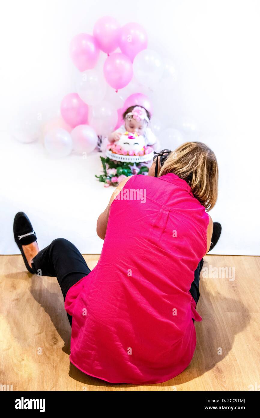 Ritratto verticale di un fotografo che scatta foto della torta di una bambina distruggi il primo compleanno in uno studio. Foto Stock