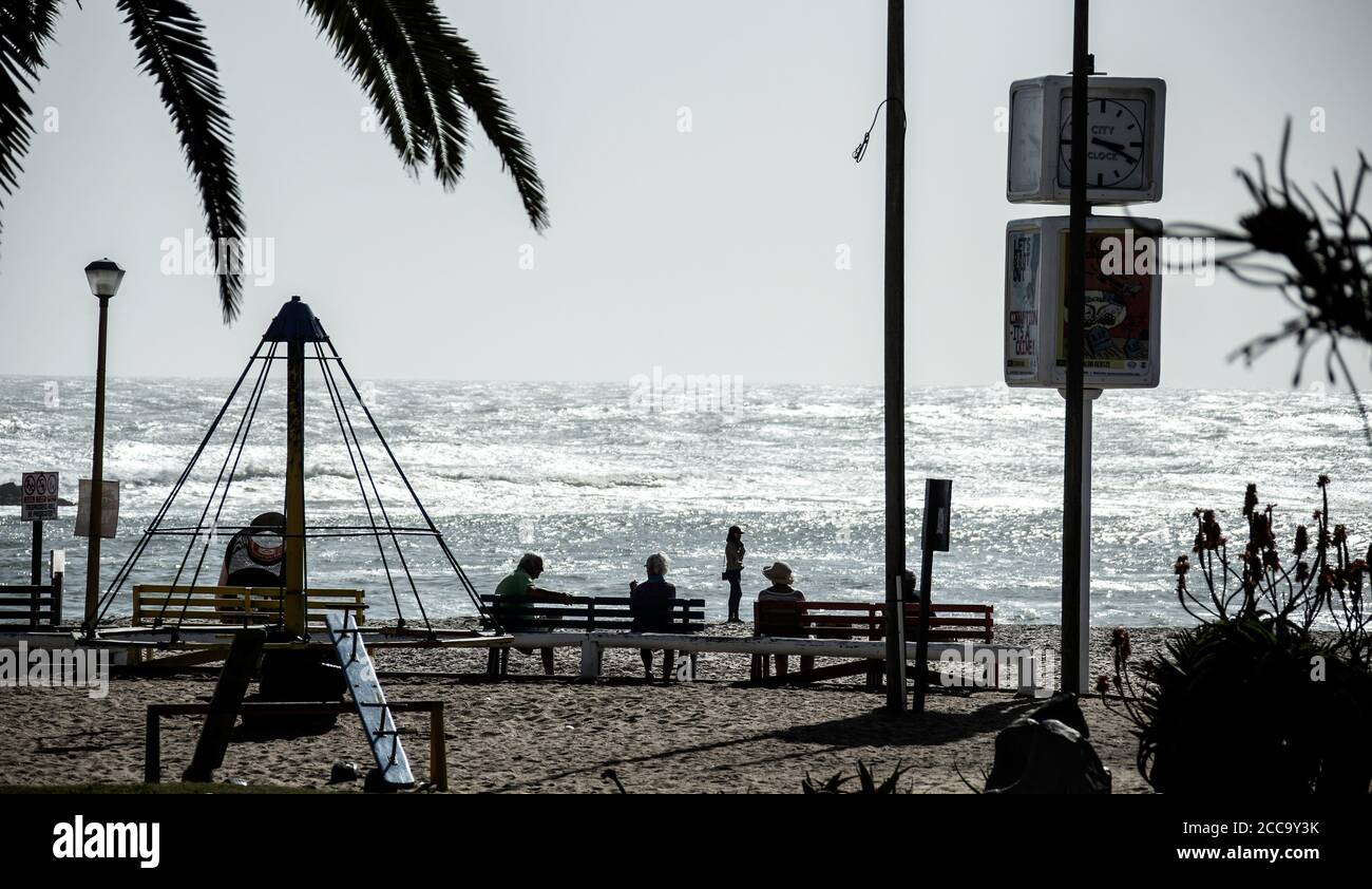Individui seduti su panchine e divaricarsi dal mare Foto Stock