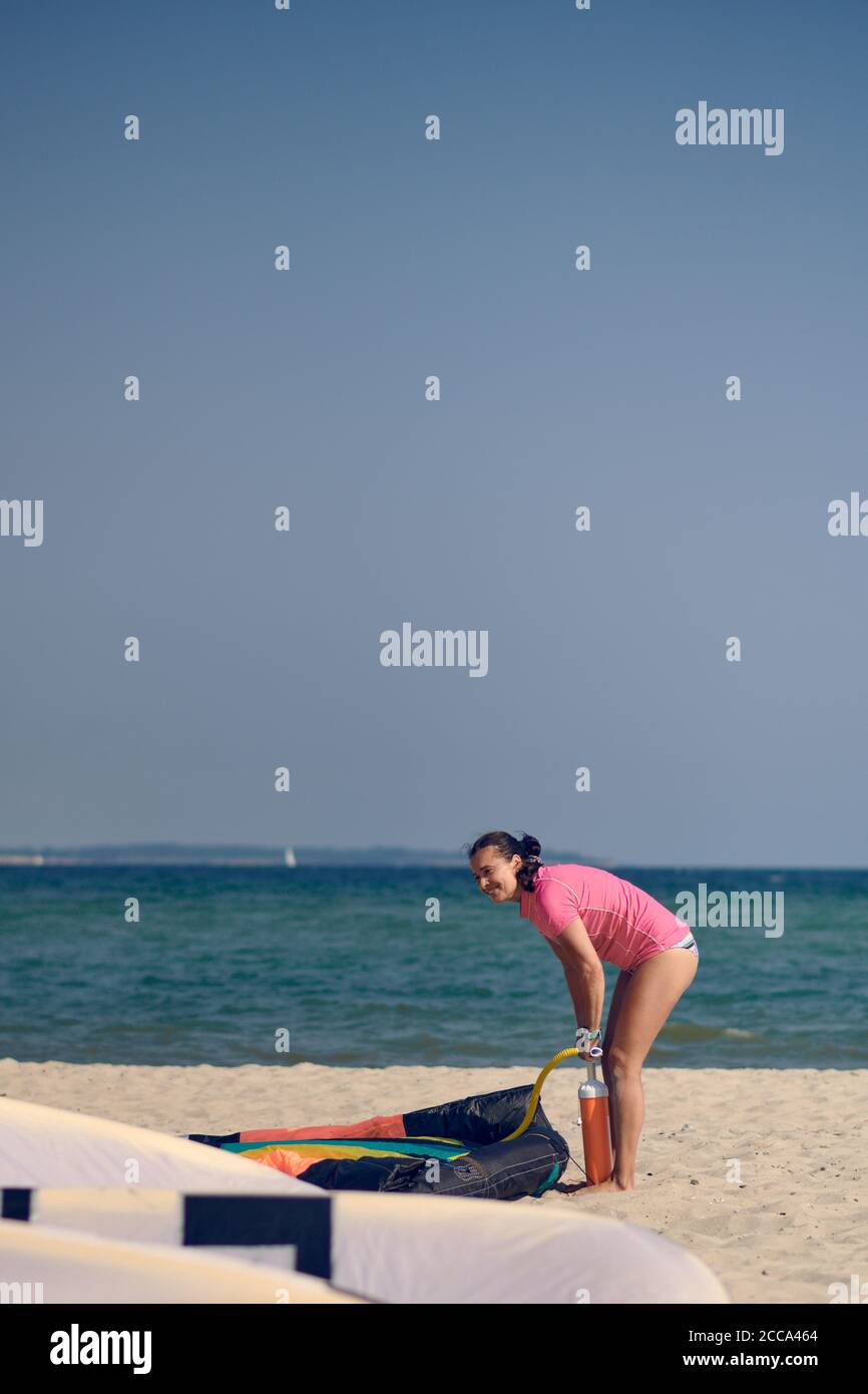 Donna di mezza età che pompa un kitesurf kite al spiaggia in vacanza estiva in sole caldo con sfondo oceano Foto Stock