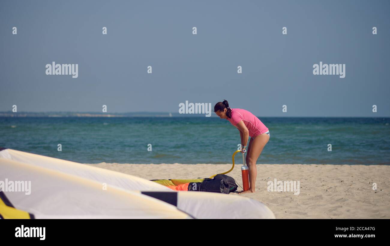 Donna di mezza età che pompa un kitesurf kite al spiaggia in vacanza estiva in sole caldo con sfondo oceano Foto Stock