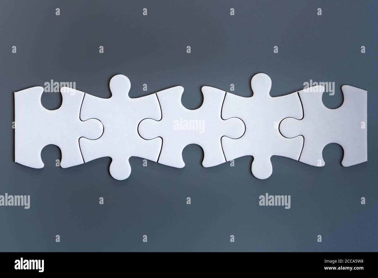 Pezzi di puzzle bianchi su sfondo grigio Foto Stock