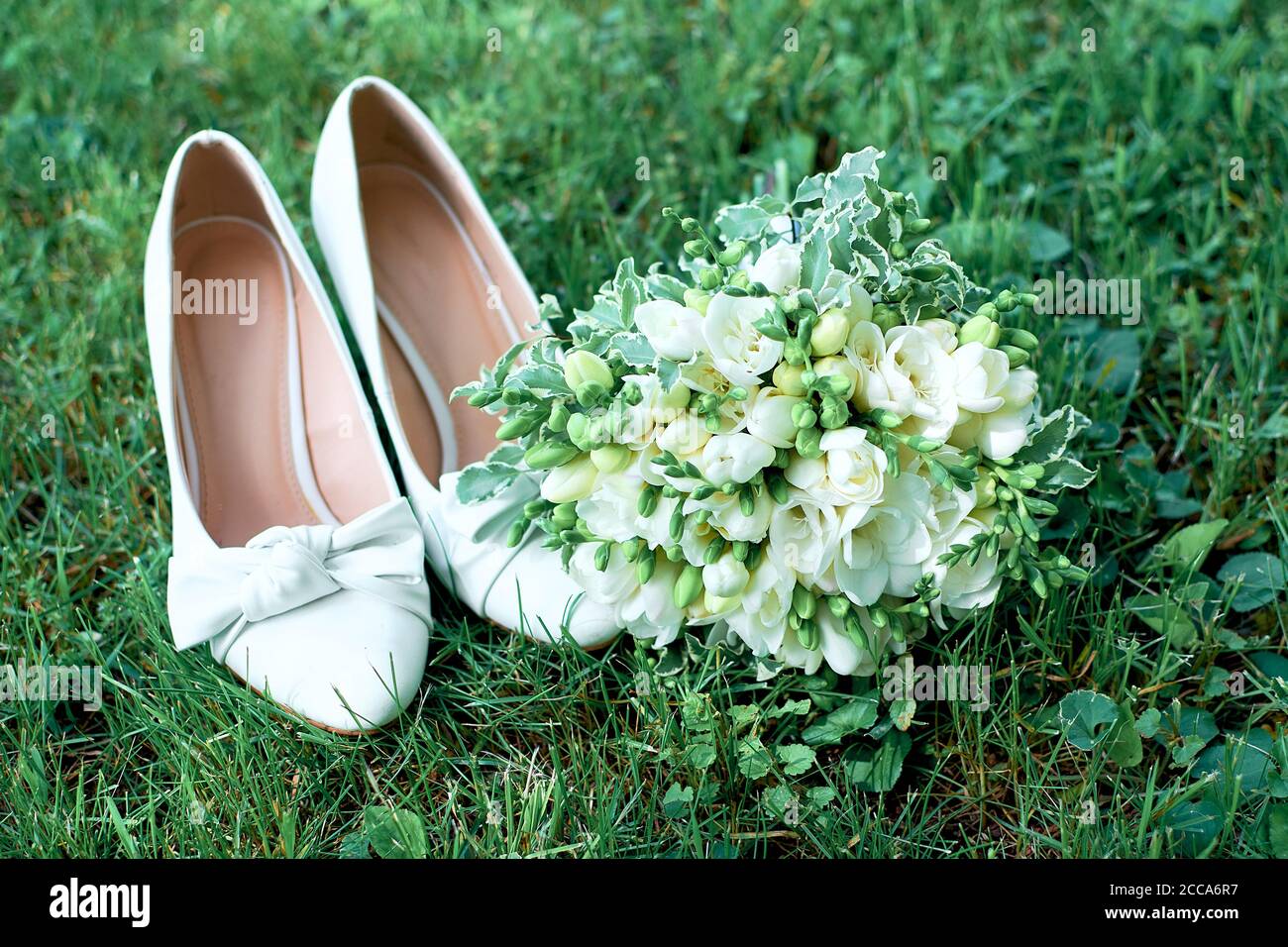 Scarpe da sposa bianche su erba verde. Bel bouquet nuziale e freesias neve-bianco Foto Stock